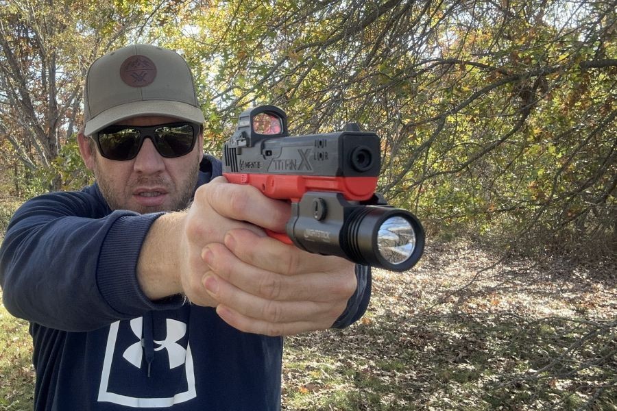 A person in a blue hoodie with a green hat, shooting an orange and black training pistol. 